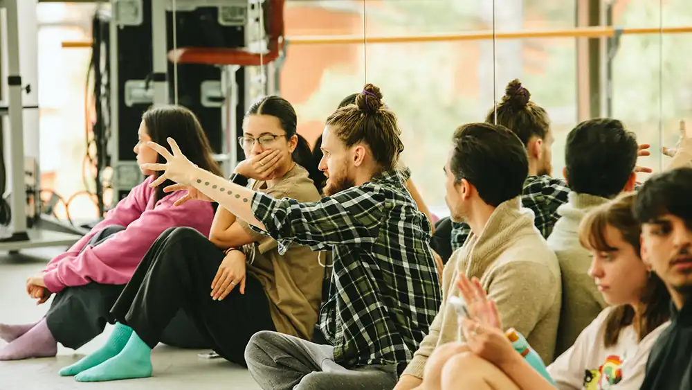 Professor speaking to the camera in a classroom style class, with her hands opened.