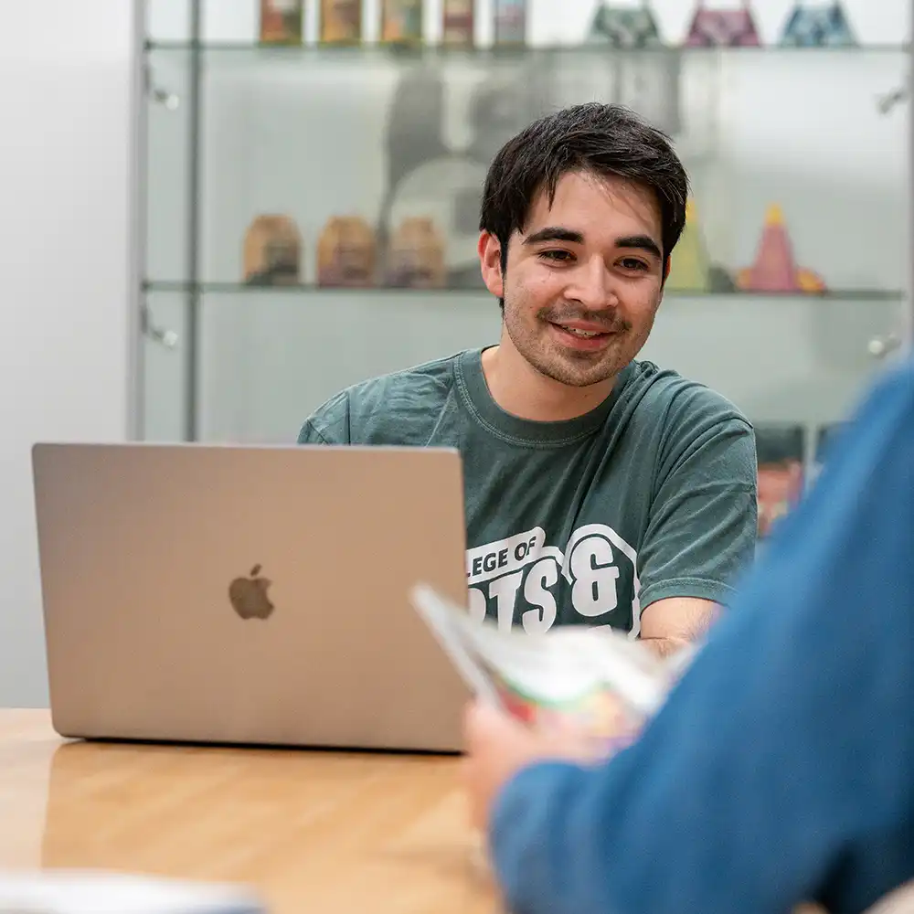 Two women looking at each other, smiling, sitting down, working on an assignment.