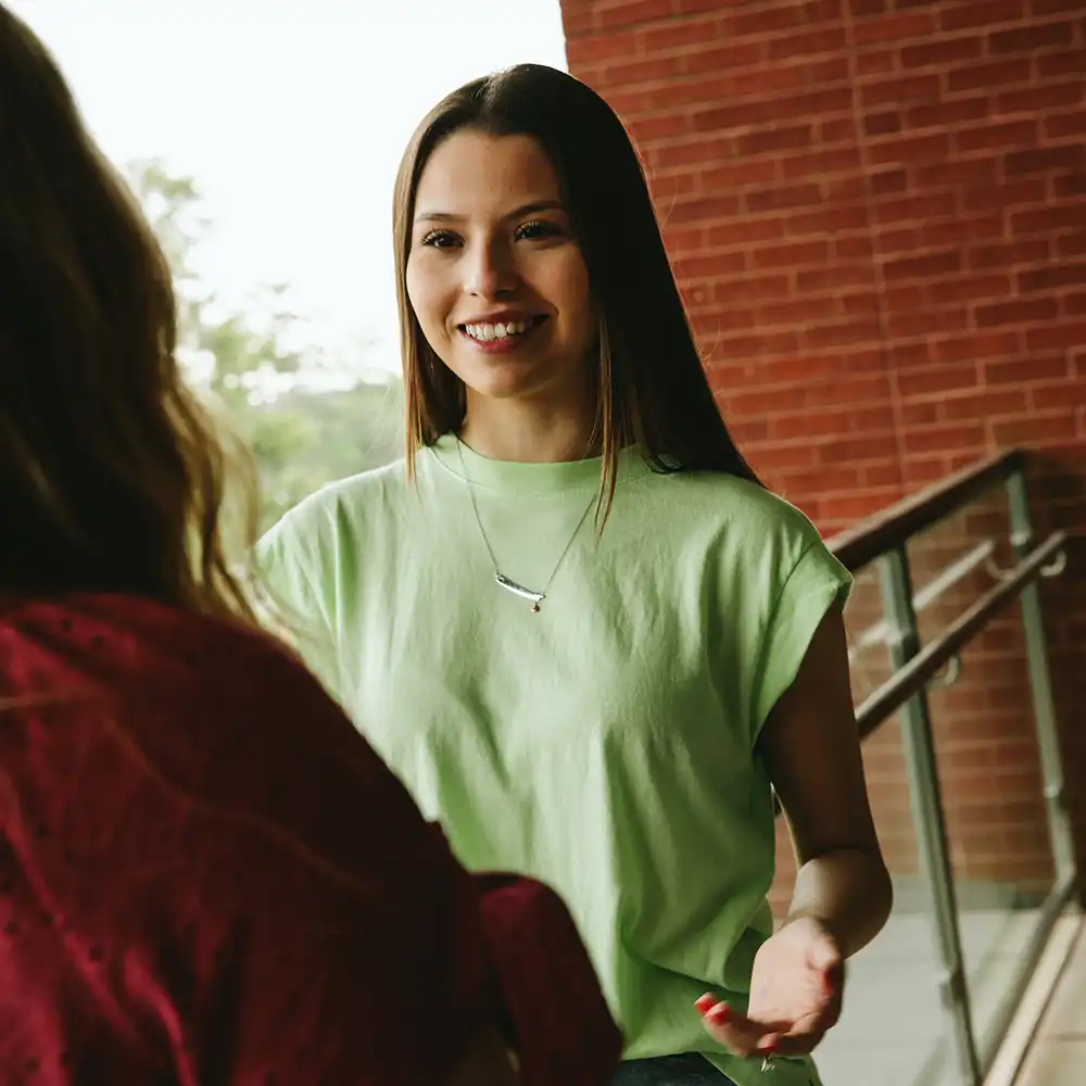 Two women looking at each other, smiling, sitting down, working on an assignment.