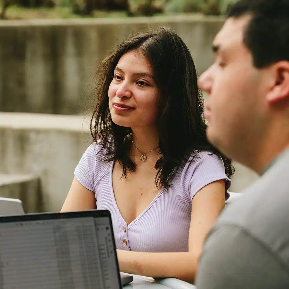 Two women looking at each other, smiling, sitting down, working on an assignment.