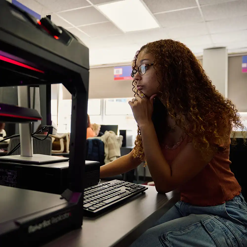 Student works on a project with computer and 3d printer in IRIS Suite.