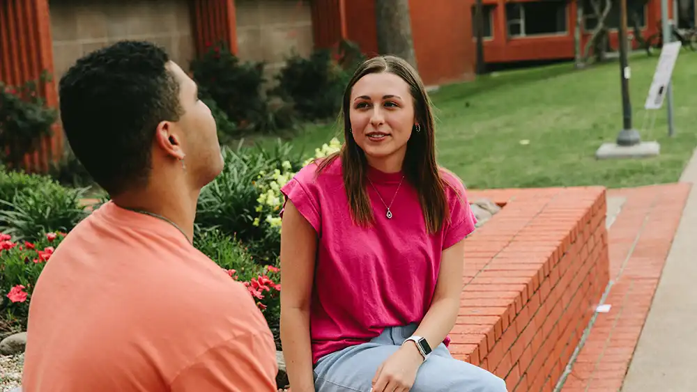 Professor speaking to the camera in a classroom style class, with her hands opened.