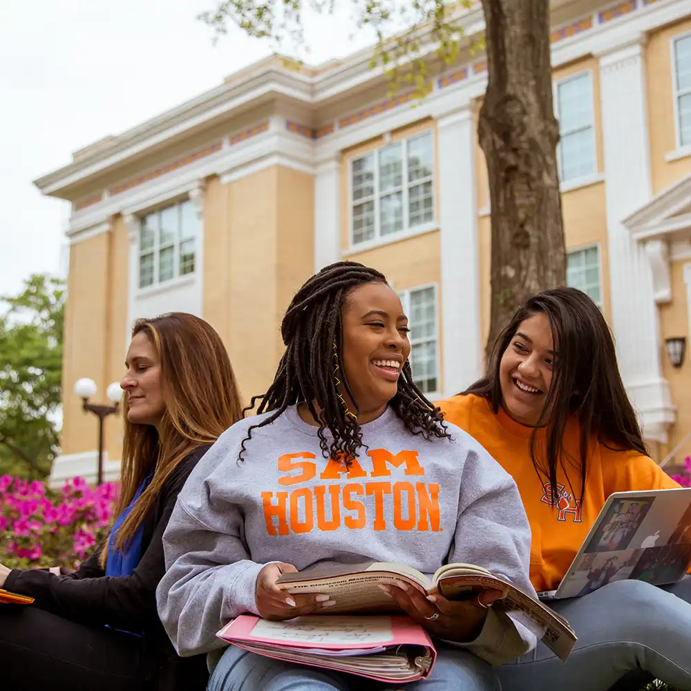 Two women looking at each other, smiling, sitting down, working on an assignment.