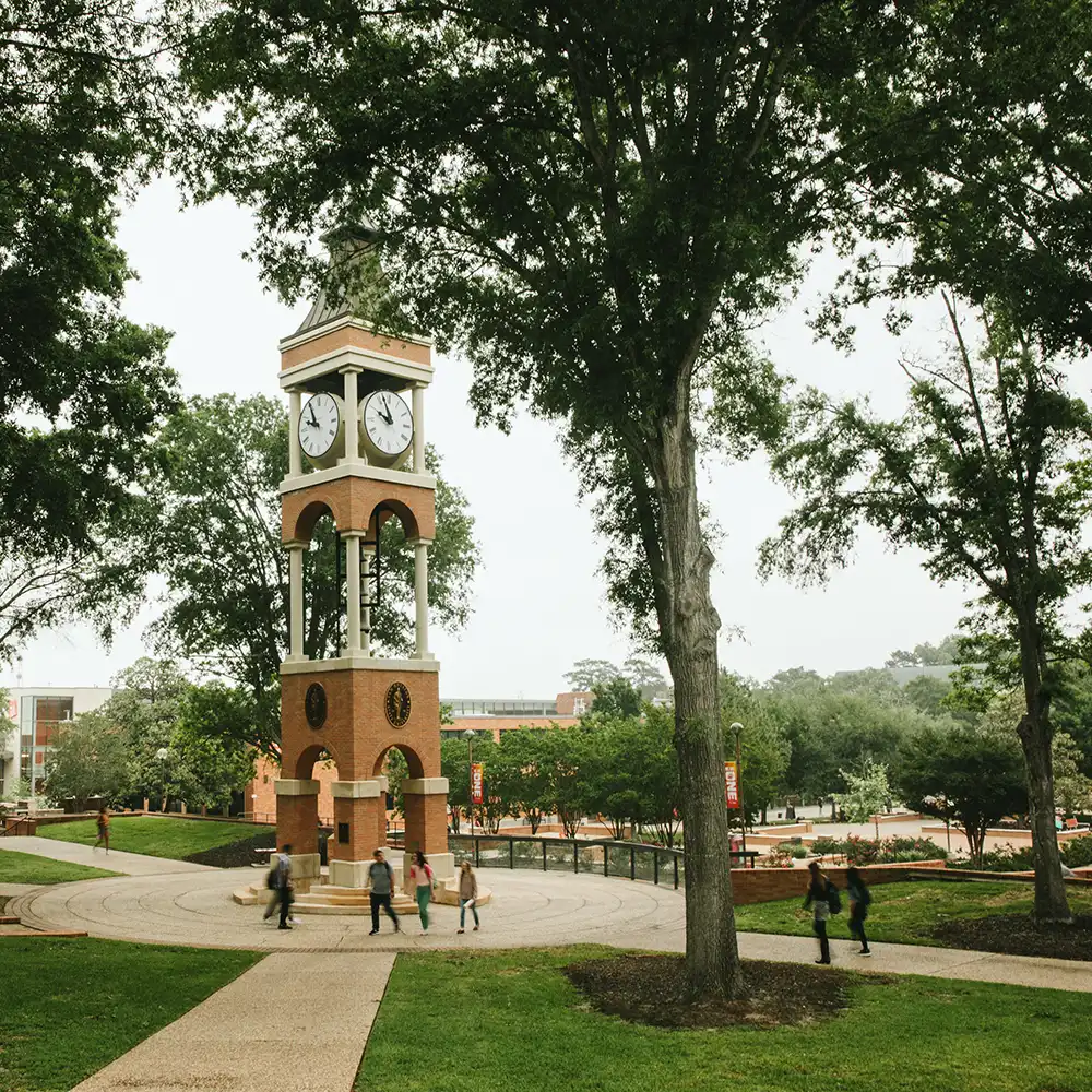 SHSU student stands in front of clock tower on campus smiling and looking confident.