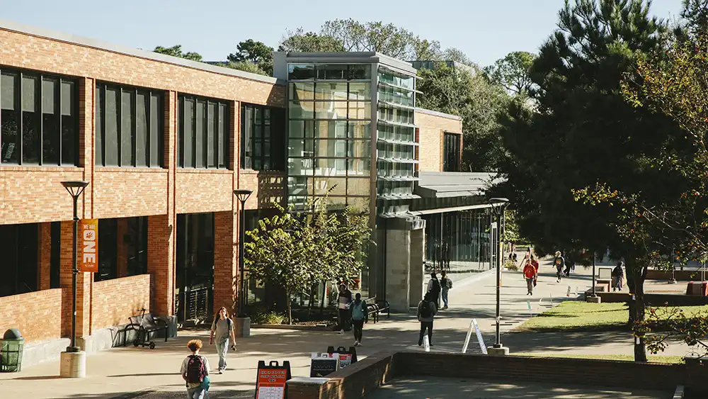 Professor speaking to the camera in a classroom style class, with her hands opened.
