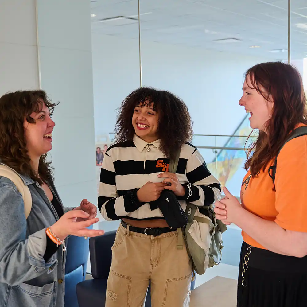 Two women looking at each other, smiling, sitting down, working on an assignment.