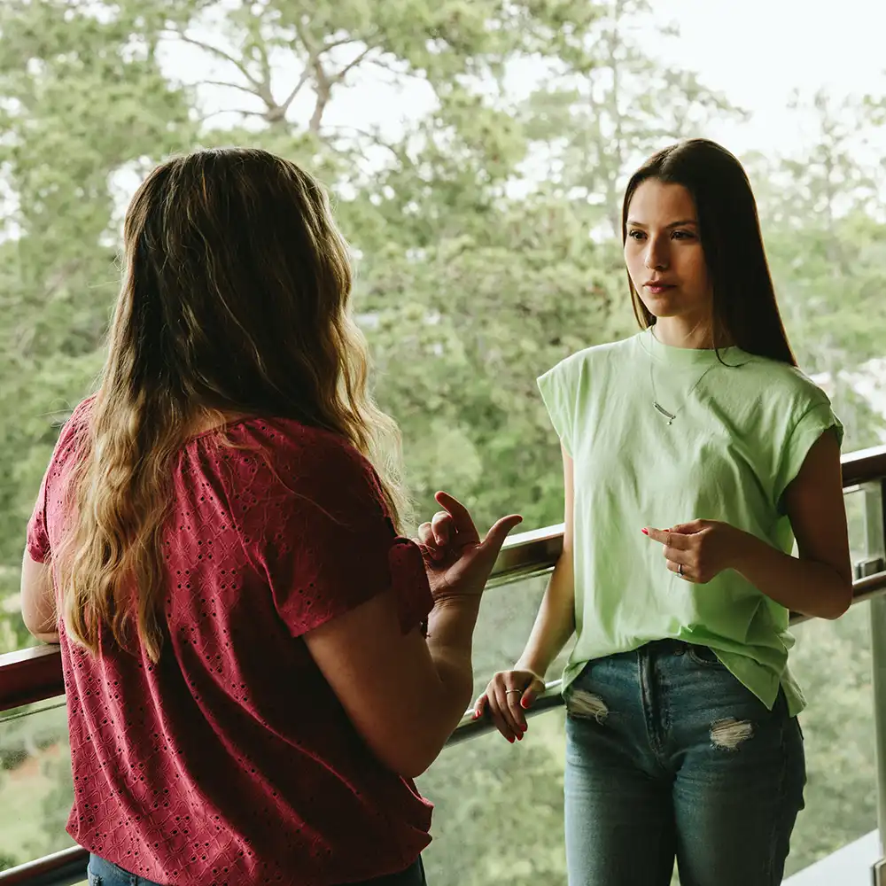 Two women looking at each other, smiling, sitting down, working on an assignment.