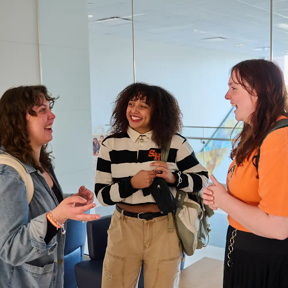 Two women looking at each other, smiling, sitting down, working on an assignment.