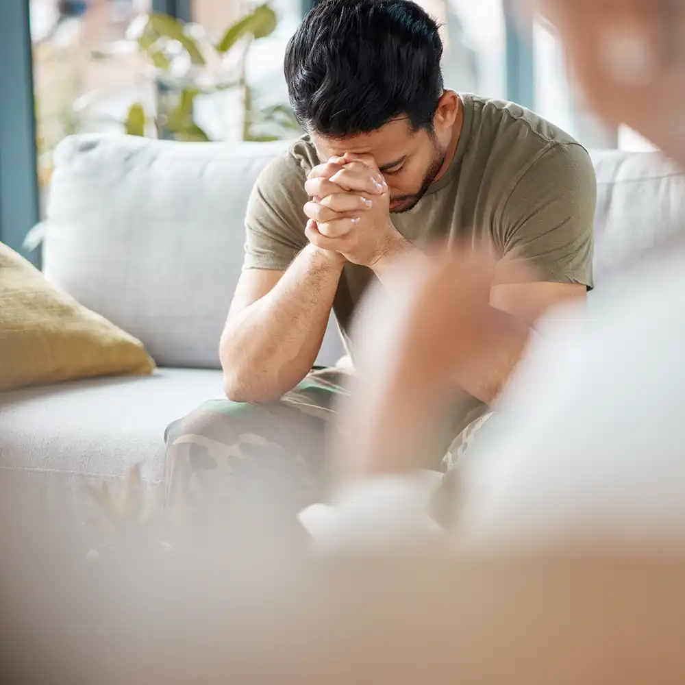 Man with head down, hands clasped, in thought. 