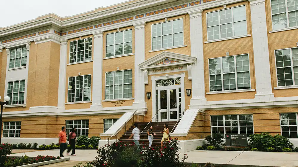 Professor speaking to the camera in a classroom style class, with her hands opened.