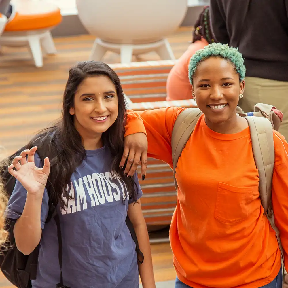 Two women looking at each other, smiling, sitting down, working on an assignment.