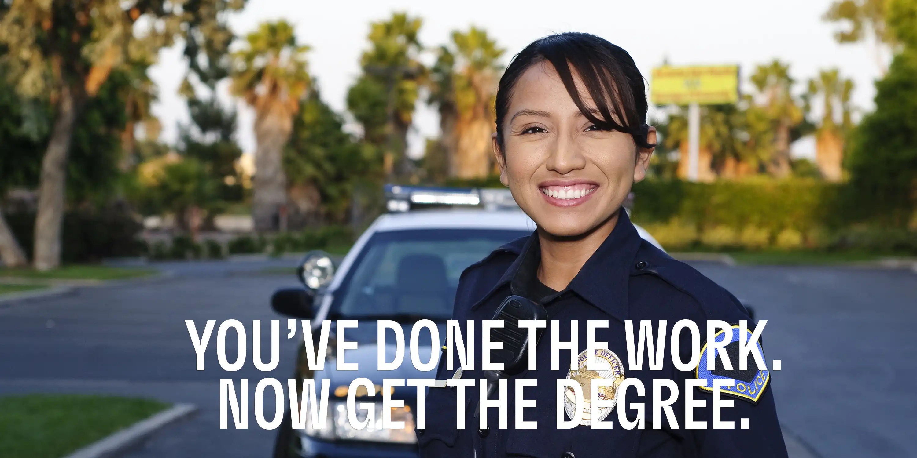 Smiling woman in police uniform in front of police car in background with text overlay that reads, "You've Done the Work. Now Get the Degree."