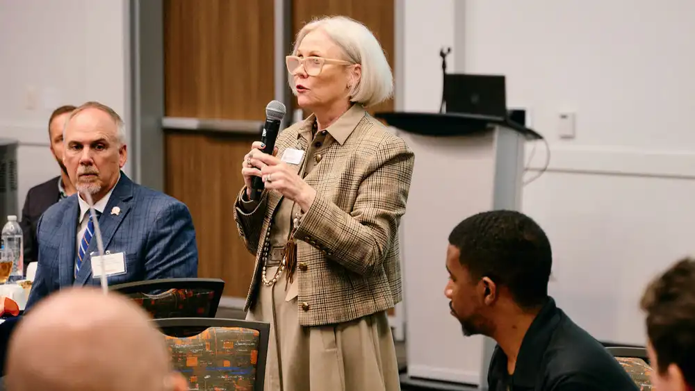 Professor speaking to the camera in a classroom style class, with her hands opened.