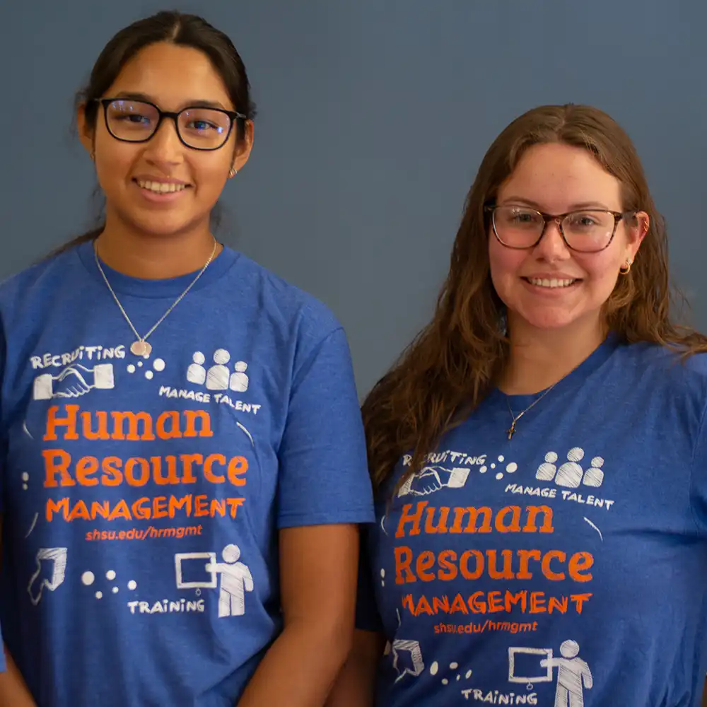 Two women looking at each other, smiling, sitting down, working on an assignment.
