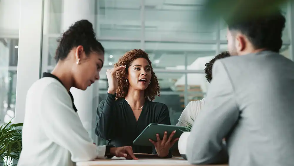 Woman sharing with two other people while holding a computer.