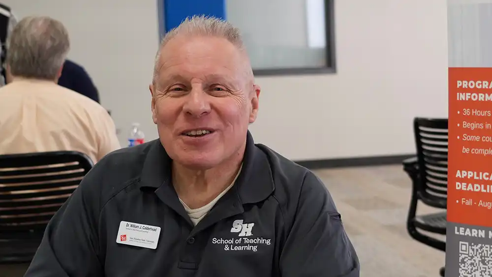 Professor speaking to the camera in a classroom style class, with her hands opened.