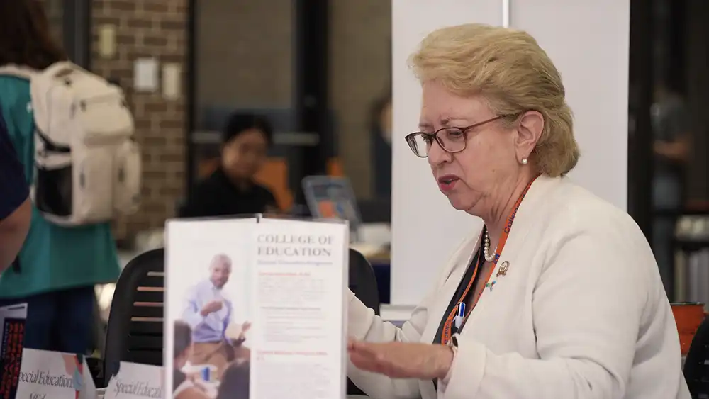 Professor speaking to the camera in a classroom style class, with her hands opened.