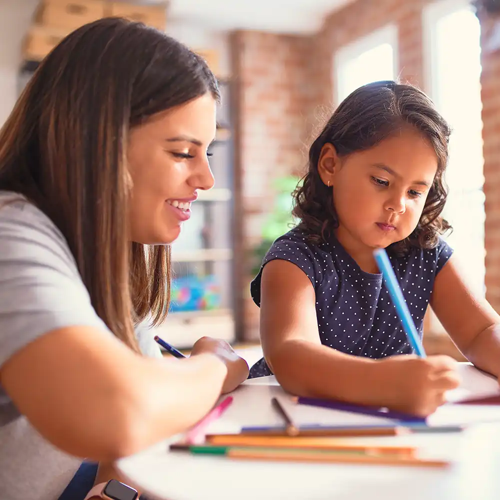 Two women looking at each other, smiling, sitting down, working on an assignment.