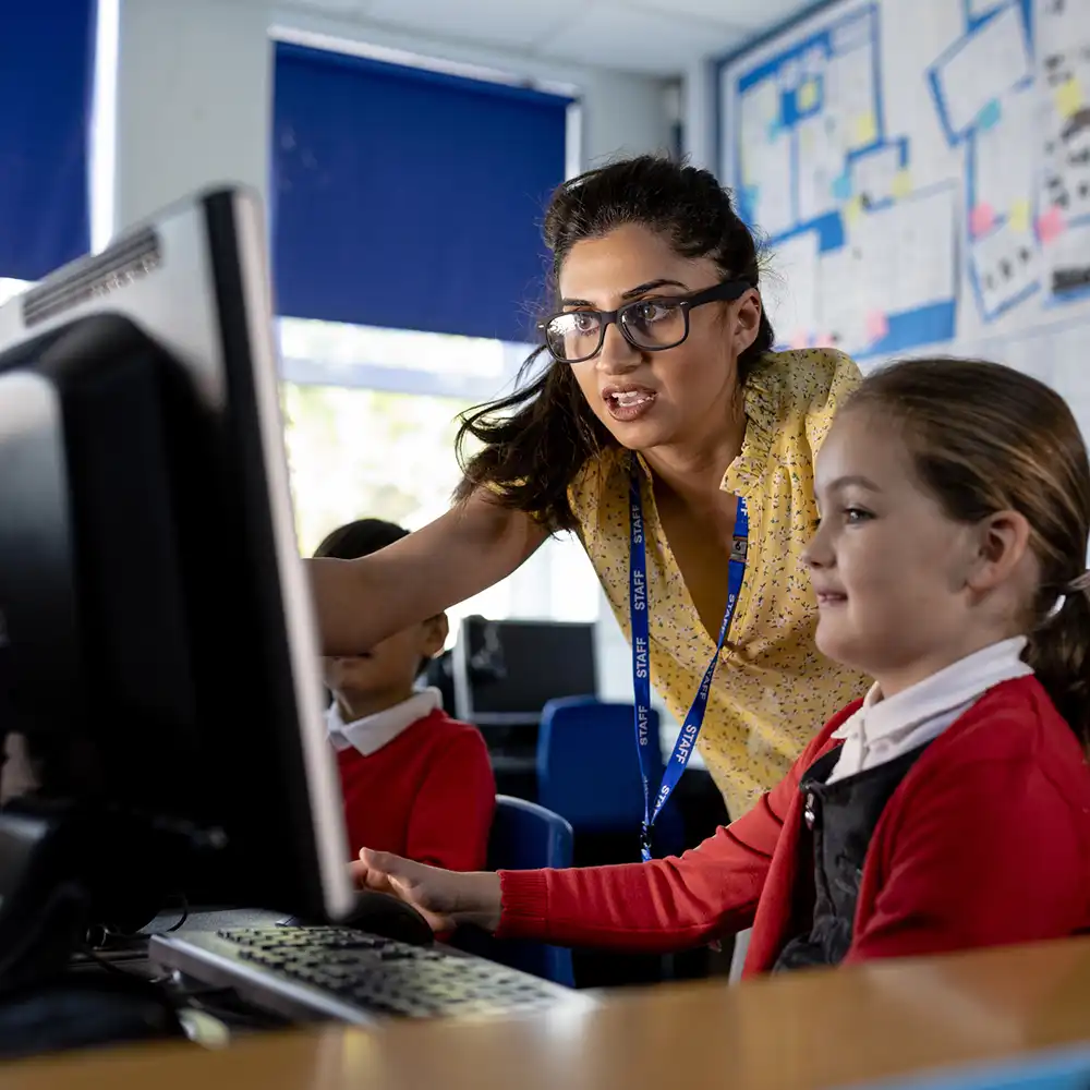 Teacher working with a young student on her computer.