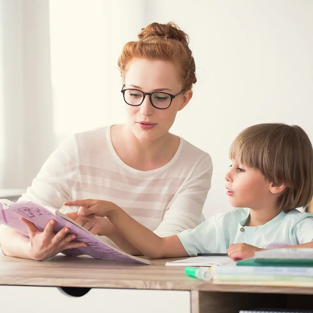Two women looking at each other, smiling, sitting down, working on an assignment.