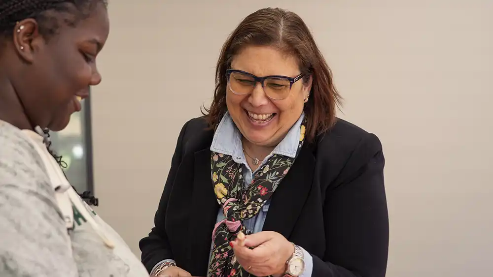 Female professor smiling and talking to a student while handing her a pen