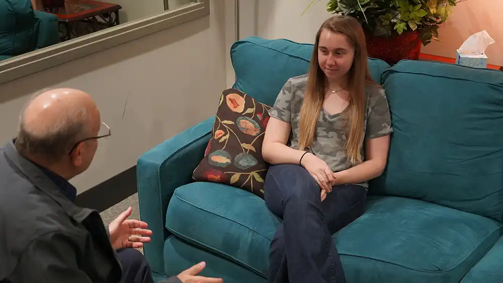 Man speaking to client, while he is holding a pen and notebook on his lap, while she is sitting in a wheelchair
