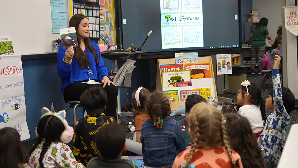 Teacher speaking to her students who are sitting down around her while she has a card in her hands