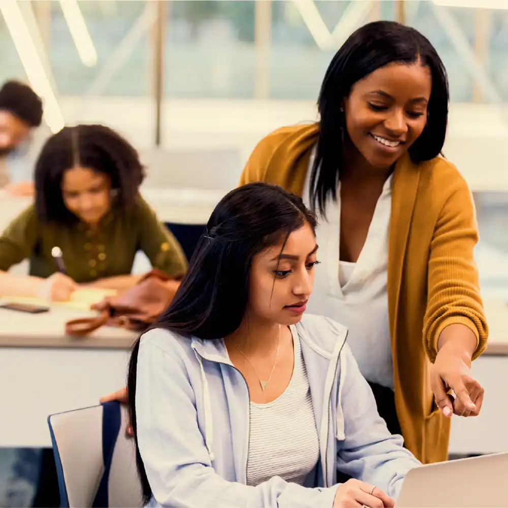 Female teacher standing over a student’s shoulder pointing to a computer screen