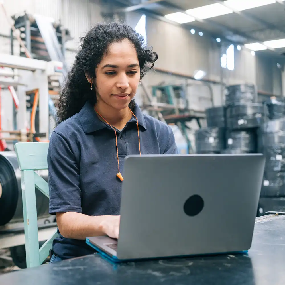 Student working on laptop in manufacturing plant.