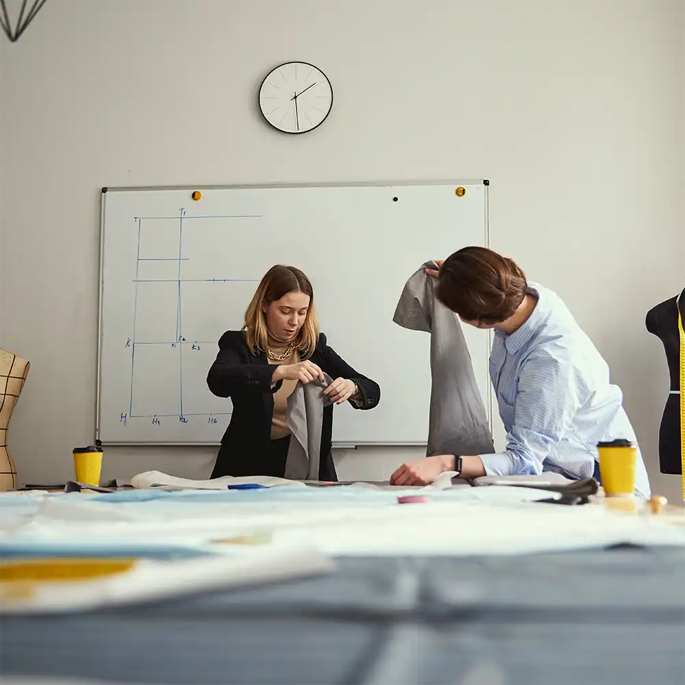 Two women looking at each other, smiling, sitting down, working on an assignment.