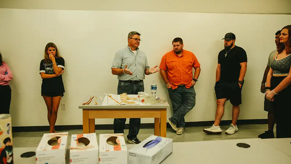 Professor speaking to the camera in a classroom style class, with her hands opened.
