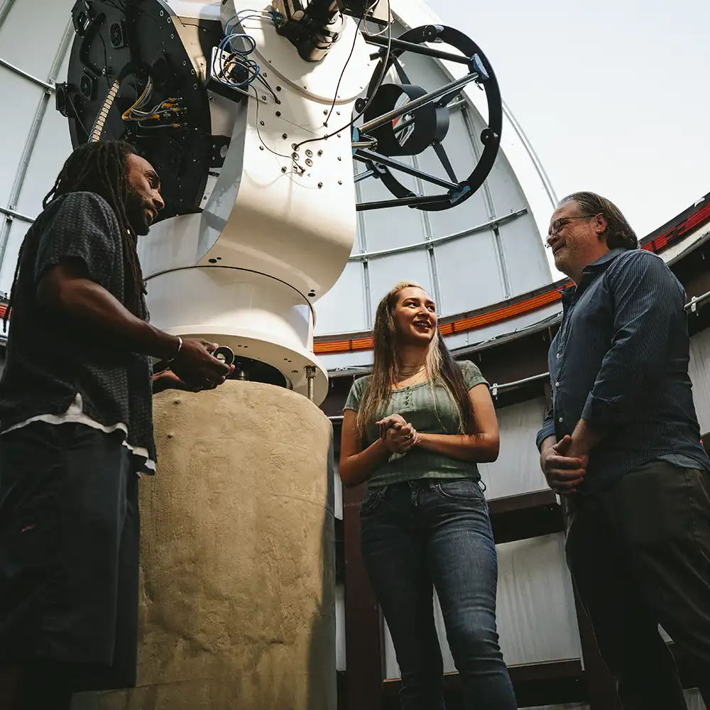 Two women looking at each other, smiling, sitting down, working on an assignment.