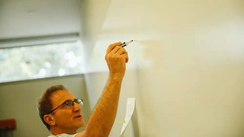 Professor speaking to the camera in a classroom style class, with her hands opened.