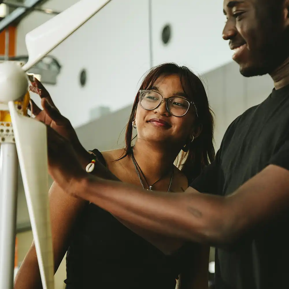 Two women looking at each other, smiling, sitting down, working on an assignment.