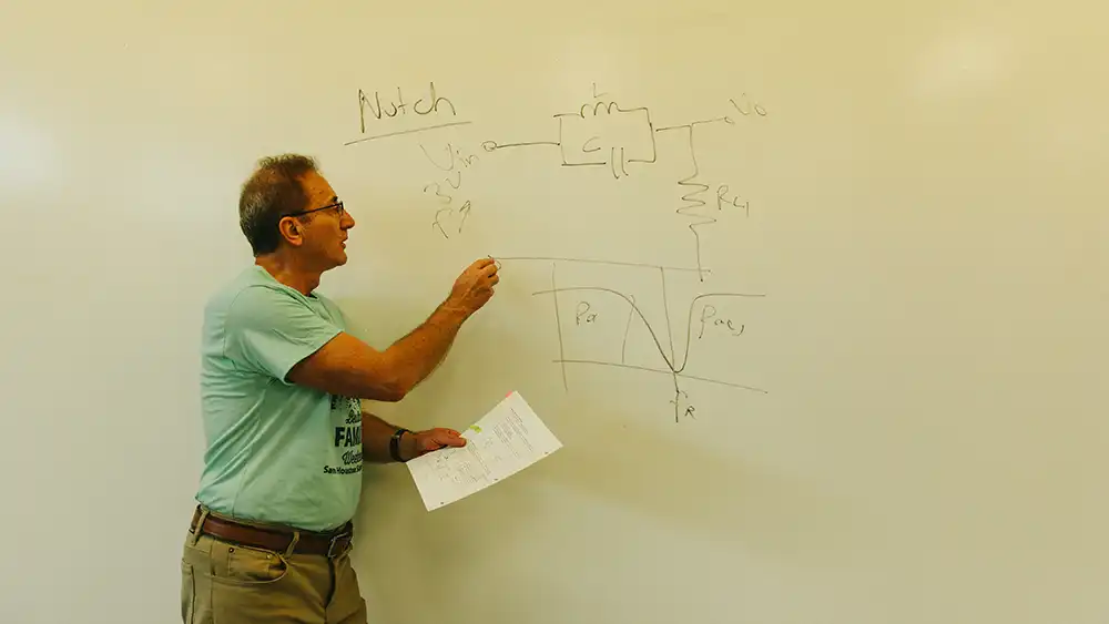 Professor speaking to the camera in a classroom style class, with her hands opened.