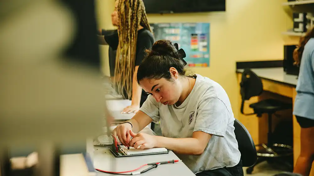 Professor speaking to the camera in a classroom style class, with her hands opened.