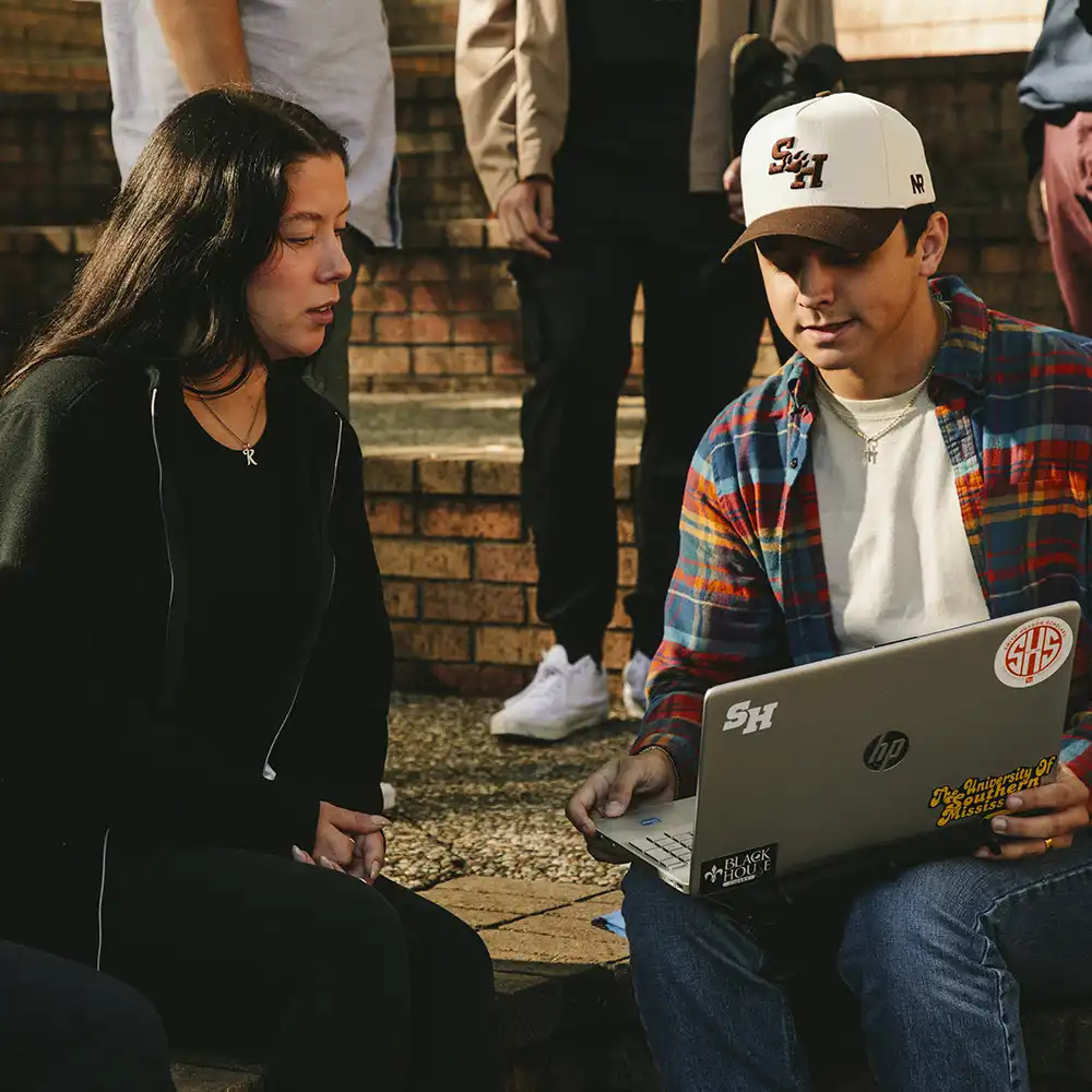 Two students looking at a laptop in the quad.