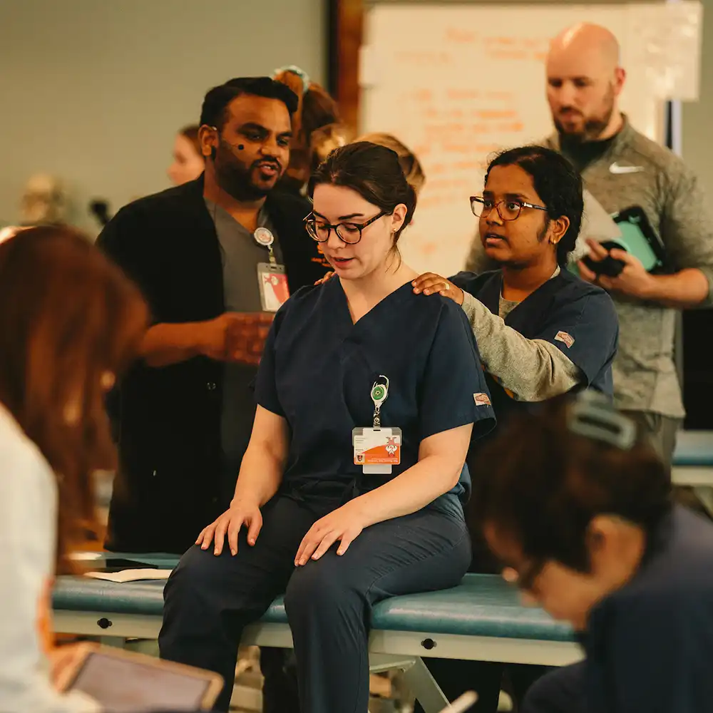 Group of seven students standing next to each other in a line in scrubs in front of windows