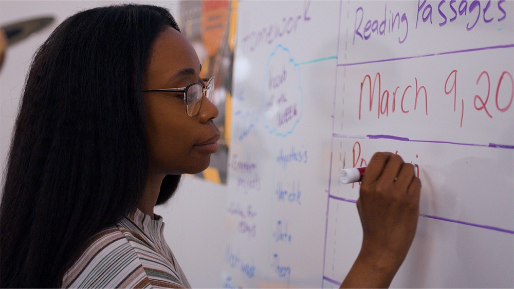 Teacher writing on a whiteboard with a red marker.