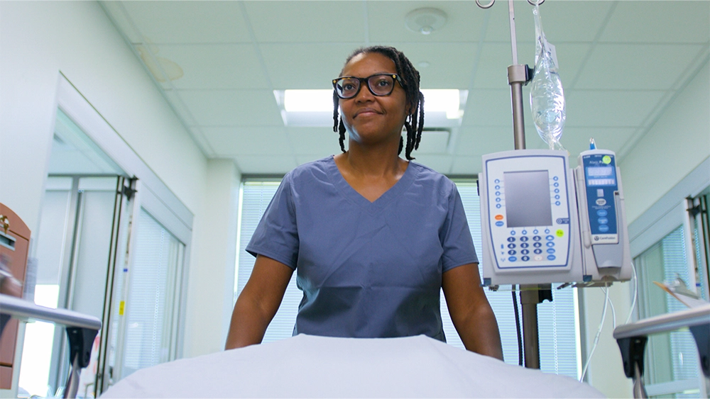 Female nurse pushing a patient's bed down a hallway, looking up toward the end of the hallway.