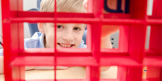 A little boy looks through a gird that holds alphabet blocks.
