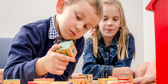 A boy and girl play with alphabet blocks.