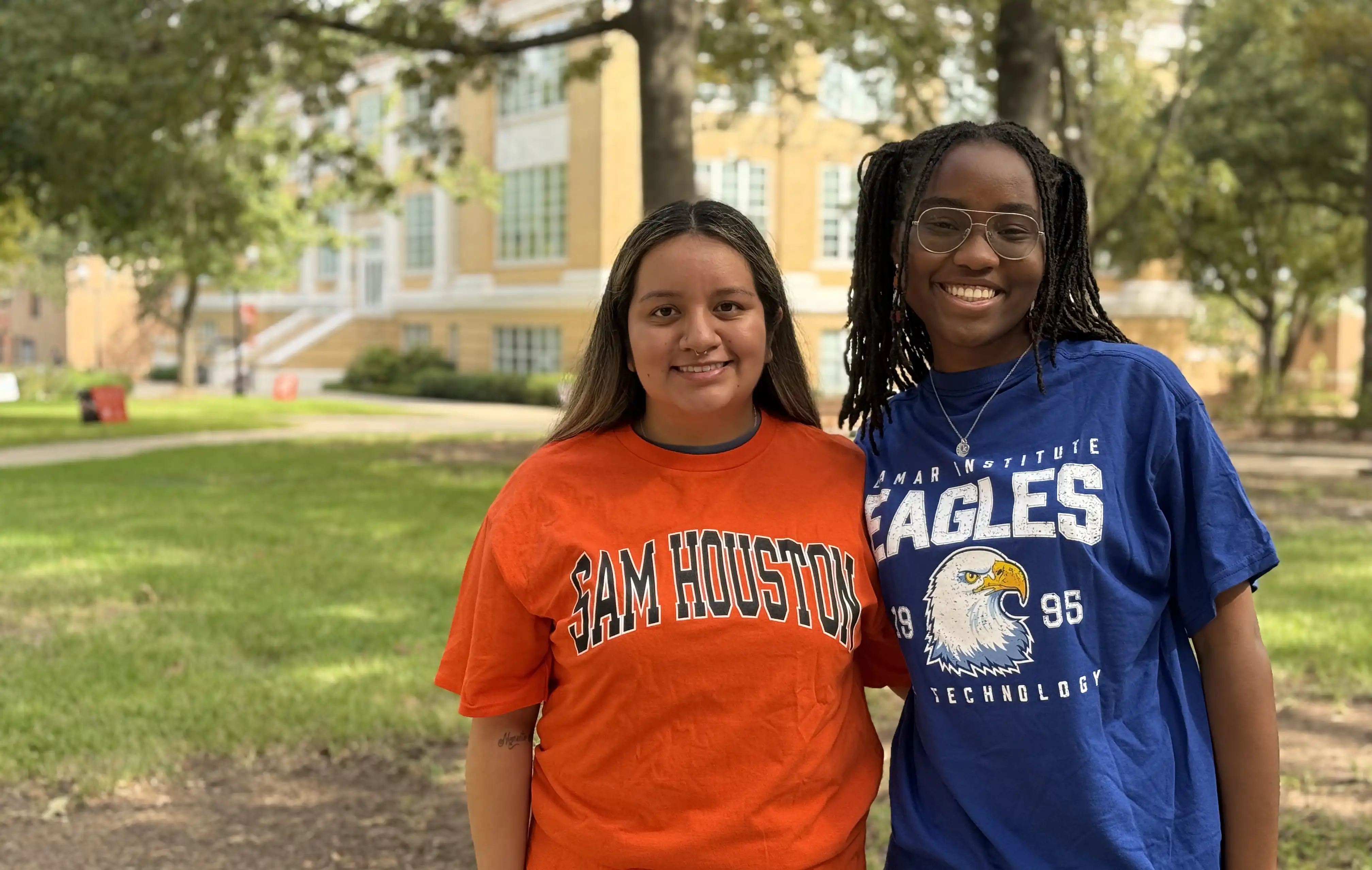 Two smiling students standing outdoors on campus wearing orange SHSU shirt and a LIT shirt posing together during a student event.