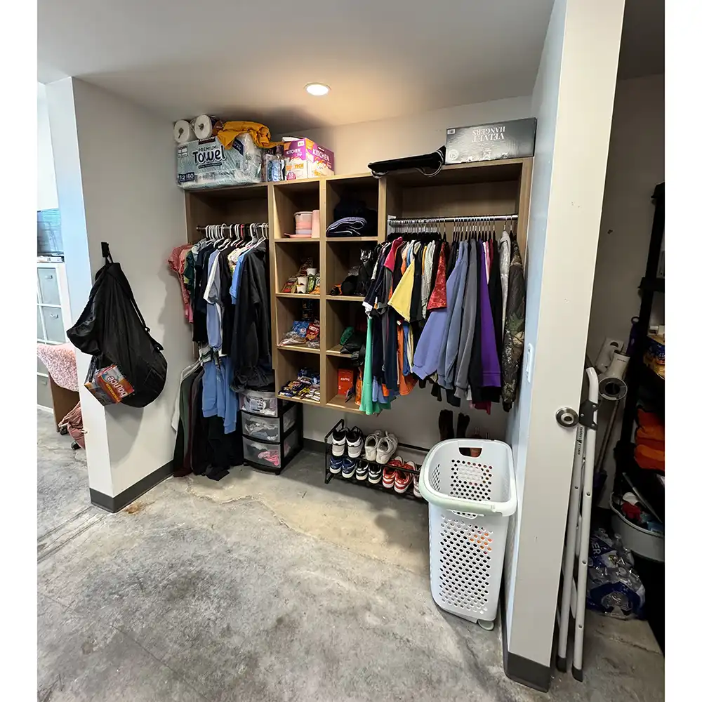 Organized closet space in SHSU’s San Jacinto Hall featuring open wooden shelving with hanging clothes, cubbies filled with snacks and supplies, shoes neatly lined at the bottom, storage bins, and a laundry basket.