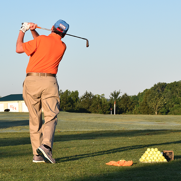 Golfer with orange shirt mid swing.