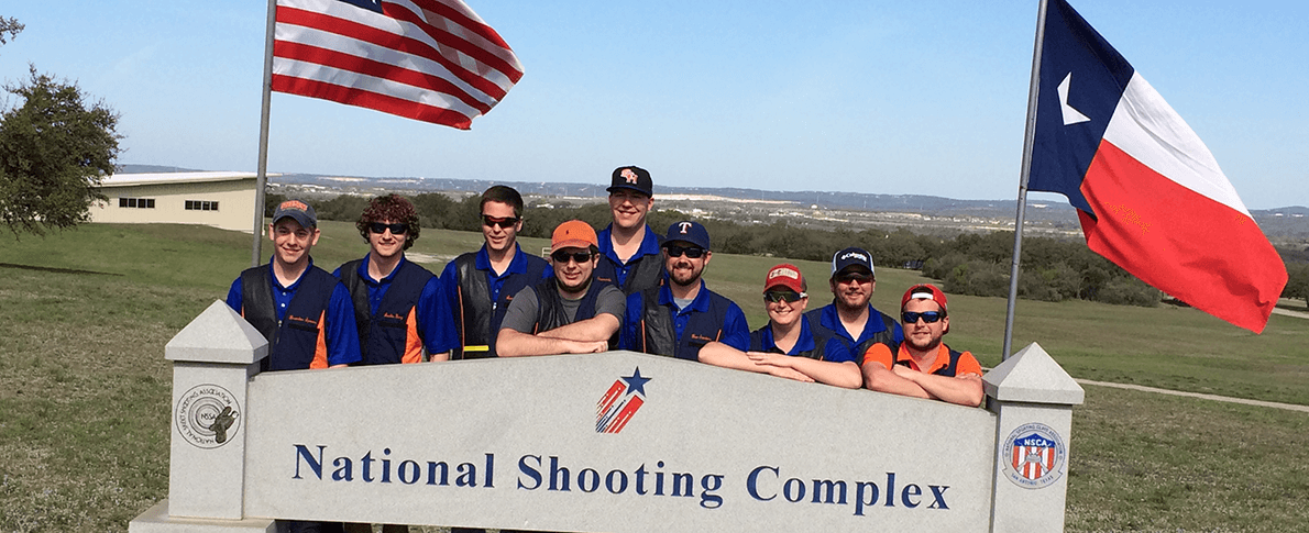 Trap Skeet team kneeling behind National Shooting Complex sign
