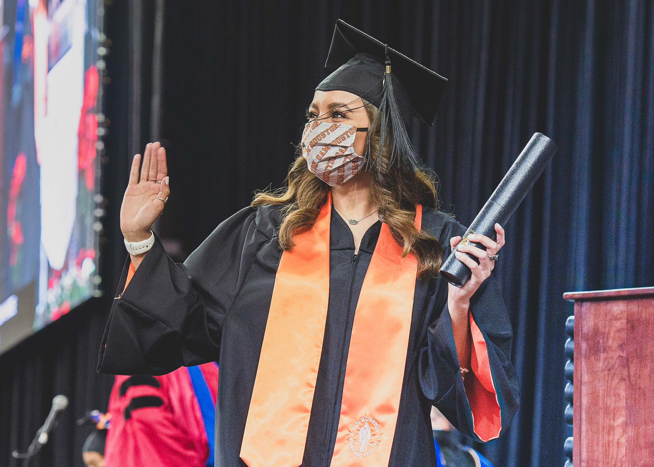Student standing on Commencement stage holding a diploma and waving