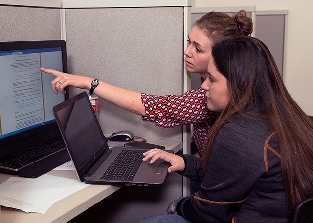 Advisor points to a computer screen and a student looks at a laptop.