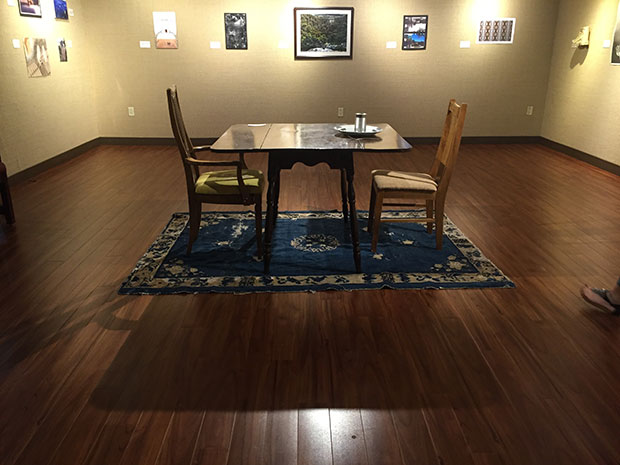 student art work a square dining table with two chairs placed on opposite sides, one place setting, and a blue persian style rug underneath the table and chairs