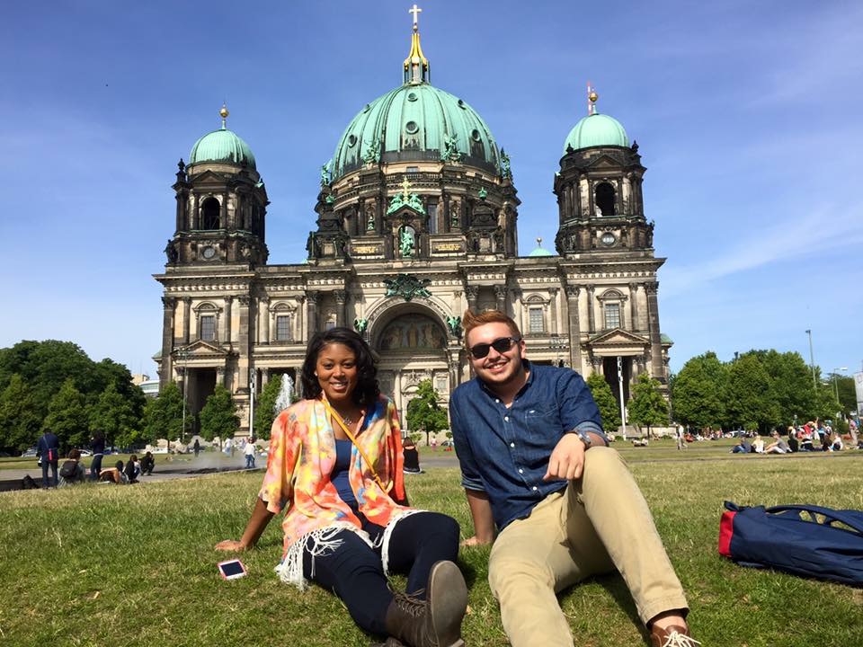 Cesar and a classmate sitting on a hill in front of a Gothic style building in Europe